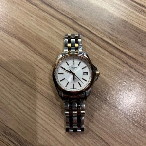 Certina DS Prime klocka - Elegant Certina DS Prime klocka med en stilren vit urtavla och datumvisning. Klockan har en tvåfärgad länkarmband i silver och guldtoner, vilket ger en lyxig känsla. Perfekt för den som söker en tidlös accessoar med en modern touch.