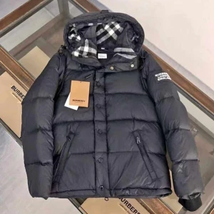 Svart dunjacka från Burberry - Snygg svart dunjacka från Burberry med avtagbara ärmar och huva. Jackan har en klassisk rutig insida och dragkedja samt knappar framtill. Perfekt för kyliga dagar.