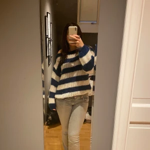 Randig stickad tröja från Design by Si - Mysig stickad tröja från Design by Si i blått och vitt. Tröjan har ett randigt mönster och är långärmad med en offshoulder-design. Jättebra till vintern eller fina sommarkvällar 💗