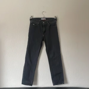 Svarta jeans från Tommy Jeans - Snygga svarta jeans från Tommy Jeans med en klassisk design. De har en slim passform och är perfekta för en stilren look. Jeansen har en knappgylf och är tillverkade i ett slitstarkt material. De passar mig som e 179.