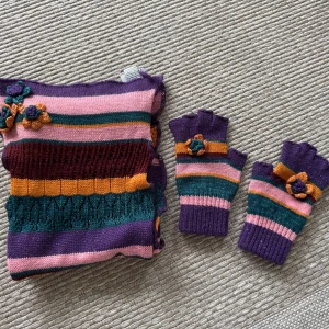 Randig halsduk och handskar från Dolce & Gabbana Junior - Säljer en färgglad randig halsduk från Dolce & Gabbana Junior. Halsduken har ränder i lila, rosa, orange och grön med glittriga detaljer och blommiga applikationer. Original, inköpt i Italien, mycket begränsat använda. 1650kr för båda. 