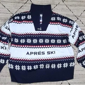 Mönstrad tröja från Esmara - Säljer en snygg tröja från Esmara med texten 'APRÈS SKI'. Tröjan har ett vinterinspirerat mönster i blått, vitt och rött med snöflingor och dragkedja vid halsen. Perfekt för kyliga dagar!