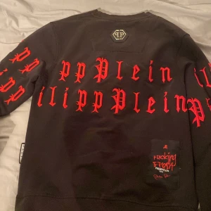 Svart tröja från Philipp Plein med röd text - Snygg svart tröja från Philipp Plein med röd gotisk text över hela framsidan och ärmarna. Tröjan har en rund halsringning och ett märke med PP-logga på ryggen. Perfekt för en cool och edgy stil. Inte helt säker på nypris men tror de var runt 5500kr men mitt pris är 899kr. Mvh Damian 