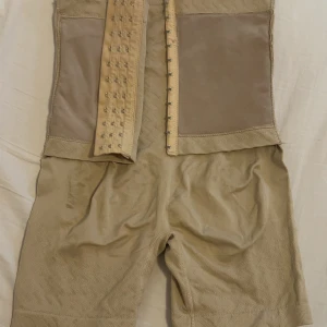 Beige midjekorsett - Säljer en beige midjekorsett med hyskknäppning framtill. Den har en slät design med elastiska paneler för extra komfort och stöd. Perfekt för att forma midjan och ge en smickrande siluett. Eh använd funkar för M ochså