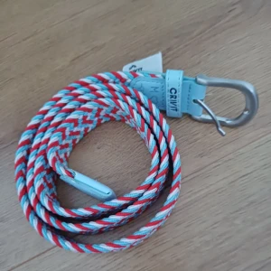 Bälte - Snyggt bälte från Crivit i en flätad design med färgerna röd, blå och vit. Bältet har ett silverfärgat spänne och detaljer i ljusblått material. Perfekt för att ge en färgklick till din outfit!