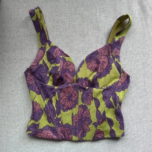 Blommig korsettopp från Zara - Jättesnygg korsettopp med blommigt mönster i lila och grönt från Zara. Är endast använd en gång och är i bra skick, dock har lappen där bak lossnat lite i sömmen som går att se på andra bilden🥰Storlek M men skulle kunna passa en S också