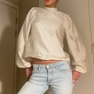 vit beige blus med puffärmar - Elegant beige blus med långa puffärmar och knäppning med knapp vid nacken. Köpt på dressingroom. Satin material men finns annat material under så den ej är genomskinlig