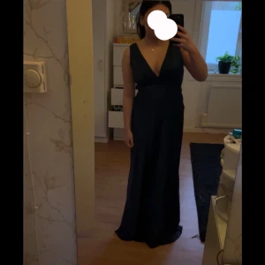 Balklänning  - Elegant mörkblå långklänning med djup v-ringning och knytning i ryggen. Produkten är i oanvänt skick och lappen sitter kvar. Säljer då jag hittat en annan. Skriv gärna för fler bilder eller pris diskussion. Passar perfekt som balklänning! Eftersom den har knytning baktill så är storleken ganska flexibel.