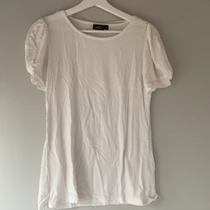 Vit blus från Kappahl - Säljer en stilren vit blus från Kappahl med korta puffärmar. Blusen har en rund halsringning och är tillverkad i ett lätt och luftigt material. Perfekt för en avslappnad och elegant look.