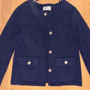 Mörkblå jacka från Hampton Republic - Snygg mörkblå jacka från Hampton Republic med guldknappar och två fickor framtill. Jackan har en rund halsringning och är tillverkad i en blandning av bomull och viskos. Perfekt för en stilren look.