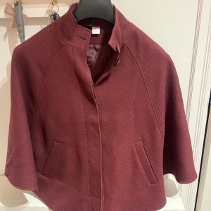 Vinröd kappa - (INTRESSEKOLL) Snygg vinröd kappa/poncho med en stilren design. Den har en hög krage och två fickor framtill. Perfekt för att ge en elegant touch till din outfit. Säljer endast för bra pris💕💕☺️