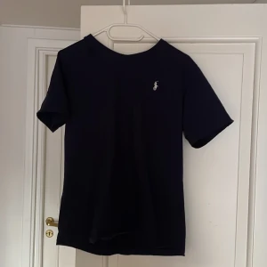 Marinblå t-shirt från Polo Ralph Lauren - Snygg marinblå t-shirt från Polo Ralph Lauren med korta ärmar och en liten broderad logga på bröstet. Perfekt för en stilren och avslappnad look till sommaren.