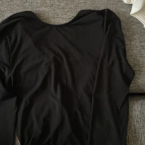 Svart långärmad topp med knyt - Snygg svart långärmad topp med knyt framtill och öppen rygg. Perfekt för en stilren look med det lilla extra. Passar bra att både klä upp och klä ner med olika stilar. 