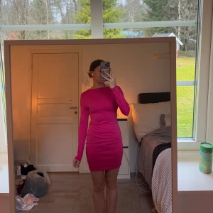 Rosa klänning med öppen rygg - Snygg rosa klänning med långärmad design och en fantastisk öppen rygg med korsade band. Perfekt för att sticka ut på festen! Klänningen är kort och har en tight passform som framhäver figuren.