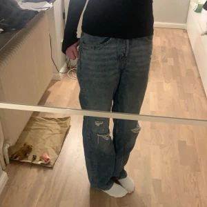 Blå jeans med slitningar - Säljer ett par blå jeans med coola slitningar. De har en loose passform och är perfekta för en avslappnad stil. Jeansen har en klassisk femficksdesign och knappgylf. (som referens är jag 175)