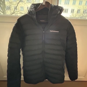 Svart dunjacka från Peak Performance - Säljer en svart dunjacka från Peak Performance. Jackan har en dragkedja framtill och är quiltad för extra värme. Perfekt för kyliga dagar med sin långa ärmar och stilrena design.