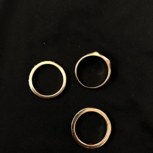 Set med guld- och svarta ringar - Säljer ett elegant set med ringar i guld och svart. Setet innehåller tre släta guldringar, en guldpläterad ring med en svart oval sten, en tunn ring med svarta stenar runt om, och en enkel svart ring. Perfekt för att mixa och matcha för olika stilar.