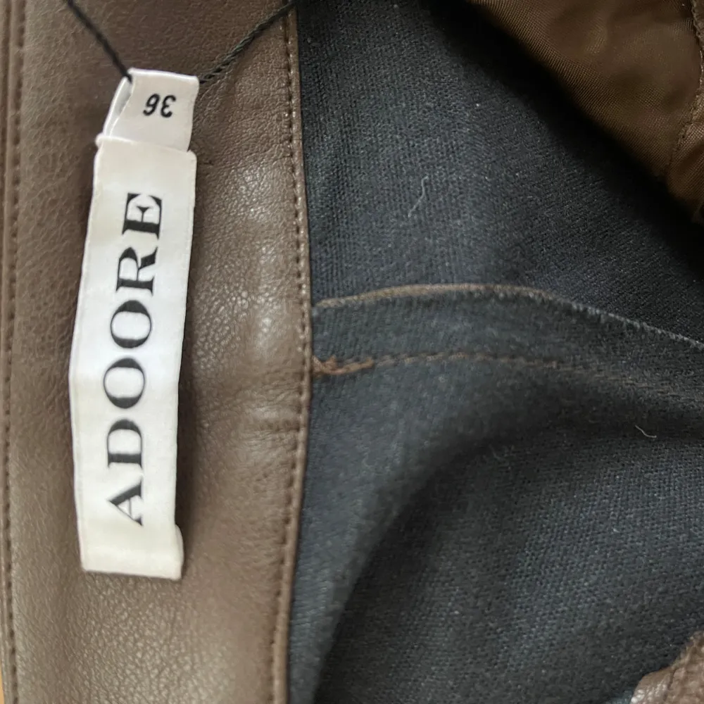 Snygga bruna skinnbyxor från ADOORE med låga midja och dragkedja . Byxorna har en bootcut-stil som ger en trendig look. Perfekta för att addera lite edge till din outfit. (Knappen har lossnat). Farkut & Housut.