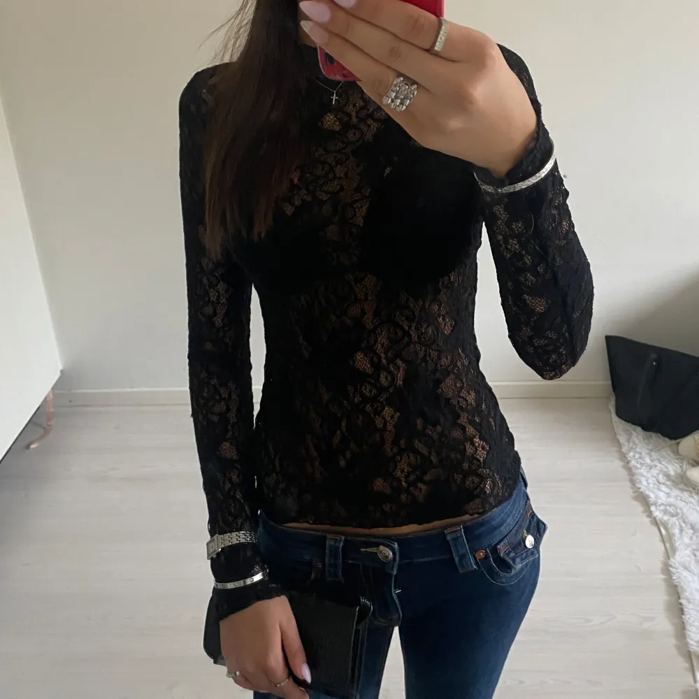 Snygg svart spetsblus med långärmad design. Perfekt för en elegant look med sitt genombrutna mönster. Blusen har en tight passform och är tillverkad i ett mjukt spetsmaterial. Den har håll i armen men det är typ inget man märker när man har på sig den . Muu.