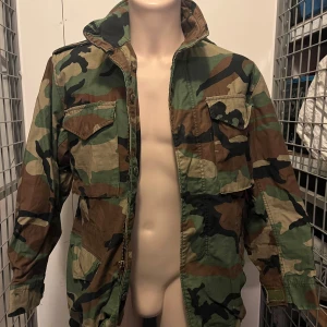 Camouflage jacka från Alpha Industries - Säljer en cool camouflage jacka från Alpha Industries. Jackan har en klassisk militärstil med dragkedja och flera fickor. Robust design och bekvämm passform.