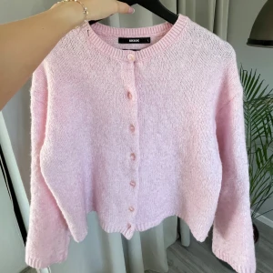 Rosa stickad kofta från BikBok - Mysig rosa stickad kofta från BikBok med knappar framtill. Perfekt för kyliga dagar och ger en söt touch till din outfit. Koftan har långa ärmar och en rund halsringning. Sitter som en S/M. Liten i storleken.