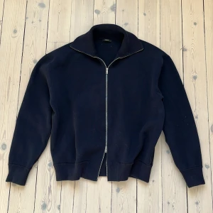 Mörkblå tröja med dragkedja från Massimo Dutti - Säljer en stilren svart tröja med dragkedja från Massimo Dutti. Tröjan har en klassisk design med långa ärmar och ribbade muddar. Perfekt för en avslappnad och snygg look.