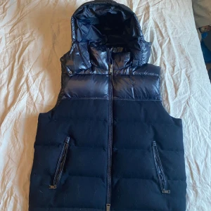 Blå dunväst från Polo Ralph Lauren - Snygg svart dunväst från Polo Ralph Lauren med dragkedja och huva. Huvan går att ta av och sätta på, finns knappar. Använd några gånger men inga fel på den! Köpt från Caliroots med nypris 5495kr.  
