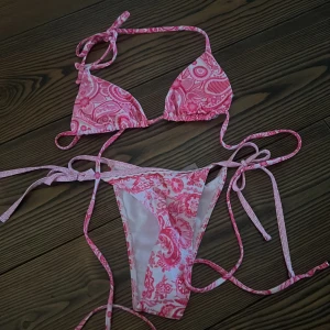 Rosa mönstrad bikini - Snygg rosa bikini med ett unikt mönster och knytband. Perfekt för sommarens stranddagar. Toppen har trekantsform och underdelen har smala knytband på sidorna.