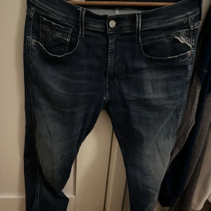 Mellanblå jeans från Replay - Snygga mellanblå jeans från Replay i storlek 32/32 med klassisk femficksdesign och diskreta slitningar. Perfekta för en avslappnad stil. Märkeslogga på baksidan. Skicket är ungefär 8/10, loggan där bak håller på och lossna lite men inga defekter utöver det. Modellen heter Replay Anbass stretch hyperflex.  Nypris ligger runt 1600-1900 men mitt pris ligger på 600 men kan diskuteras. Skriv vid frågor eller funderingar! 