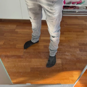 Grå jeans från Dsquared2 - Snygga grå jeans från Dsquared2 med en slim passform. De har en unik design med svarta färgstänk och ett broderat lönnlöv på bakfickan. Perfekta för dig som vill ha något annorlunda i garderoben. Priset kan diskuteras vid snabb affär.