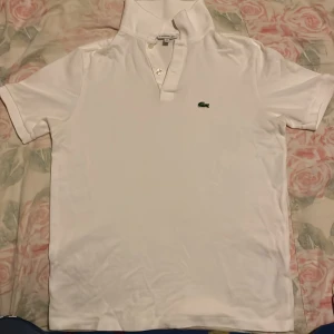 Vit pikétröja från Lacoste - Oanvänd/helt ny, säljs pga att storleken inte passar mig. Säljer en klassisk vit pikétröja från Lacoste med den ikoniska gröna krokodilen broderad på bröstet. Tröjan har korta ärmar och en stilren krage med knappar. Perfekt för en avslappnad och stilren look. Pris kan diskuteras