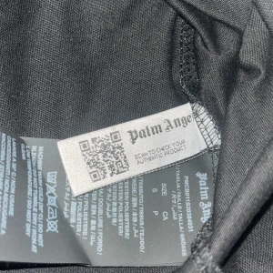 Svart t-shirt från Palm Angels - Säljer en svart t-shirt från Palm Angels med tryck i vitt och blått. Texten 'Palm Angels New York' pryder framsidan med en cool blå effekt. Perfekt för en stilren look.