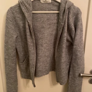 Grå hoodie från H&M - Säljer en mysig grå hoodie från H&M med dragkedja och huva tillsammans med en vit kofta från Ullared. Perfekt för kyliga dagar. De har en enkel design med ribbade muddar och fickor framtill. 50kr styck!