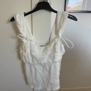 Vit linnetopp från Gina Tricot - Säljer en söt vit linnetopp från Gina Tricot. Toppen har breda axelband och knytband vid axlarna för en justerbar passform. Materialet är lätt och luftigt, perfekt för varma dagar. Nästan aldrig använd 