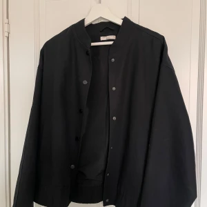 Svart jacka från Gina Tricot - Snygg svart jacka från Gina Tricot i en stilren design. Jackan har en normal passform med knappar framtill och är perfekt för både höst och vår. Den är tillverkad i ett mjukt material som ger en bekväm känsla.