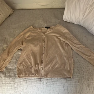 Beige kofta från Massimo Dutti - Säljer en stilren beige kofta från Massimo Dutti i storlek S. Koftan har långa ärmar och knappar framtill. Perfekt för en elegant och avslappnad look. Passar bra till både jeans och kjol.