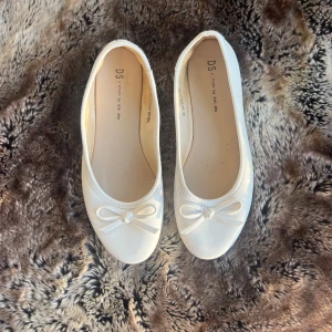 Vita ballerinaskor med rosett - Säljer ett par eleganta vita ballerinaskor från DS. Skorna har en söt rosett på ovansidan och är väldigt bekväma