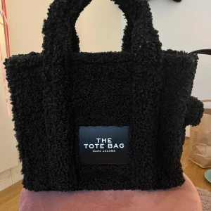 Svart tote bag från Marc Jacobs - Snygg och trendig svart tote bag från Marc Jacobs i ett teddy material. Kommer tyvärr inte till användning längre❣️ köptes för 2050, axelband tillkommer❣️ bara att skriva om ni har frågor!