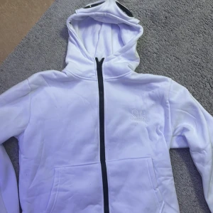Vit c.p company hoodie med glasögon storlek S - Säljer en unik vit huvtröja från C.P. Company med inbyggda glasögon i huvan. Tröjan har en dragkedja framtill och är långärmad. Perfekt för en cool och annorlunda stil.