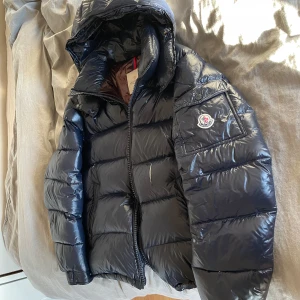 Moncler maya storlek 2 - Säljer en snygg svart pufferjacka från Moncler med glansig yta och huva. Jackan har en dragkedja framtill och Moncler-logga på ärmen. Perfekt för kyliga dagar med sin dunfyllning som håller dig varm. Finns en skada på magen på jackan som jag har lagt ut bild på! Kom privat för fler bilder o detaljer 