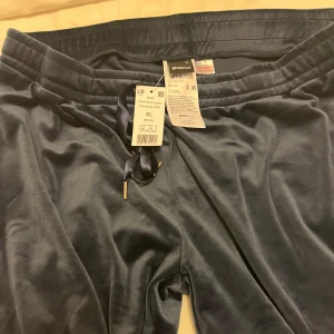 Blå mjukisbyxor från Gina Tricot - Säljer ett par bekväma blå mjukisbyxor från Gina Tricot. Byxorna har en snygg satinliknande finish och dragsko i midjan för justerbar passform. Perfekta för en avslappnad stil.