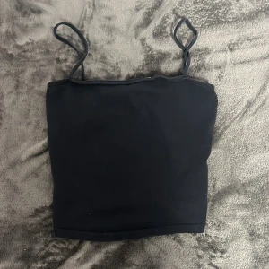 Svart linnetopp från H&M - Säljer en enkel och stilren svart linnetopp från H&M Basic. Toppen har smala axelband och en klassisk design som passar perfekt till olika outfits. Perfekt för varma dagar eller som lager under andra plagg.