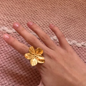Guldfärgad blomring - Snygg och iögonfallande guldfärgad ring formad som en blomma. Perfekt för att ge en extra touch till din outfit. Blomman har detaljerade kronblad som ger en elegant känsla.