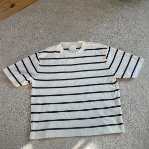 Vit och svart randig t-shirt (stickad) - Säljer en vit t-shirt med svarta ränder. Bra sick. Tunt stickad tröja, bekväm.