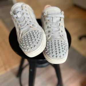 Gråa loubs med nitar - Snygga grå sneakers med nitar över hela ovandelen och hälen. Skorna har snörning och en bekväm sula. Perfekta för att ge en edgy touch till din outfit. Som du ser på bilden så har skon små hål bak i hälen, skorna går fortfarande att använda. Går säkert att fixa men jag pallar inte.