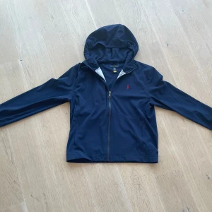 Mörkblå jacka från Ralph Lauren - Snygg mörkblå jacka från Ralph Lauren med huva och dragkedja.  Storlek Xl i barn som motsvarar S i vuxen storlek .  Pris kan diskuteras! .