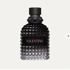 Valentino born in Roma herr parfym - Elegant parfym från Valentino i en stilren svart flaska med nitar på korken. Flaskan har en lyxig design med ett mönster av små pyramider och en etikett med rosa text. Perfekt för den som vill ha en sofistikerad doftupplevelse.