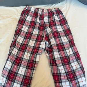 Rutig pyjamasbyxa i bomull - Mysiga pyjamasbyxor i röd, vit och svart med klassiskt rutigt mönster. Tillverkade i mjuk bomull för extra komfort. Perfekta för en avslappnad kväll hemma.