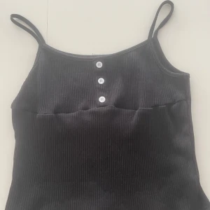 Svart ribbad linnetopp från Shein - Snygg svart ribbad linnetopp från Shein med smala axelband och tre dekorativa knappar framtill. Perfekt för en stilren och enkel look. Aldrig använd skriv för mått eller fler bilder💓💓