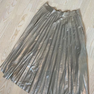 Glittrig guld kjol från Zara Woman - Säljer en superfin glittrig guld kjol från Zara Woman. Den har en elegant plisserad design och en diskret dragkedja i sidan för enkel påklädning. Perfekt för festliga tillfällen eller när du vill glittra lite extra! ✨